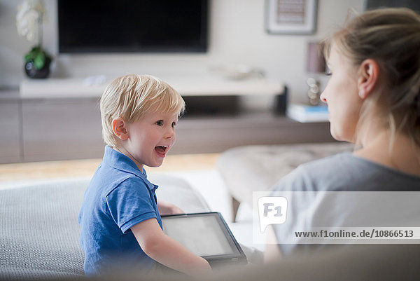 Mother and son sitting together  son holding digital tablet  laughing