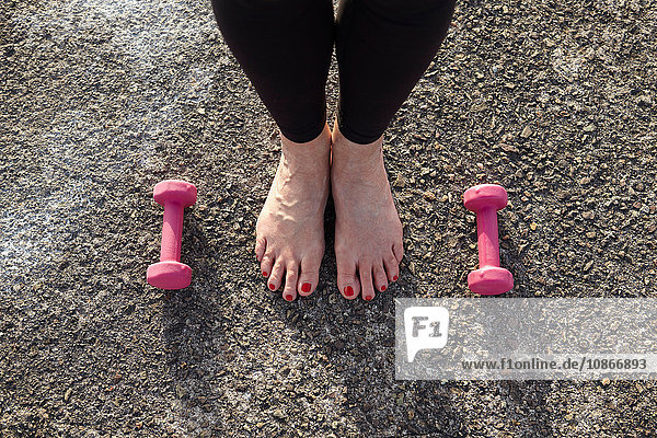 Reife Frau steht barfuß  Handgewichte auf dem Boden neben ihr  erhöhte Ansicht  Fokus auf Füße