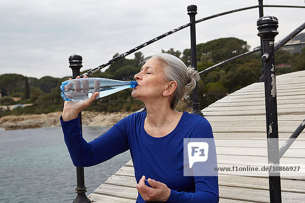 Mature woman outdoors drinking from water bottle
