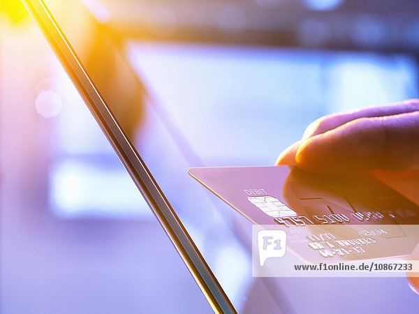 Mann benutzt seine Kreditkarte im Internet für Einkäufe und Bankgeschäfte  während Sonnenlicht durch das Fenster fällt
