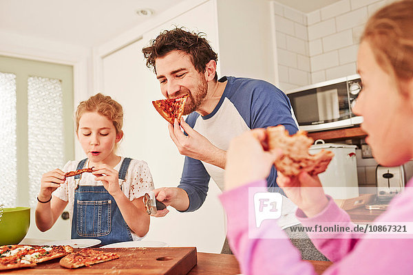 Mittelgroßer erwachsener Mann isst Pizza mit Töchtern an der Küchenbank
