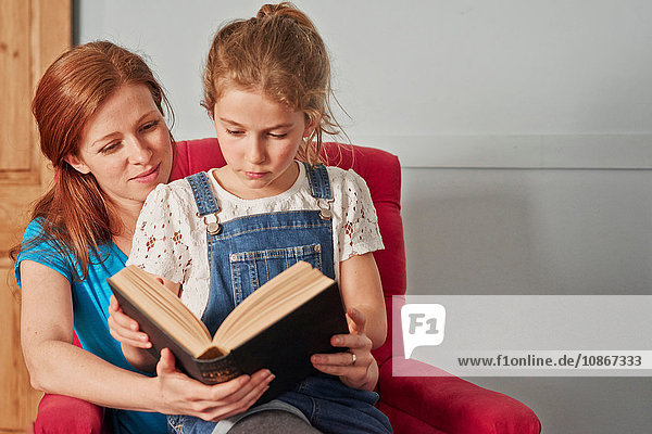 Mittlere erwachsene Frau liest Buch mit Tochter auf Sessel