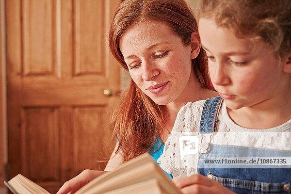 Mädchen liest Buch mit Mutter im Wohnzimmer