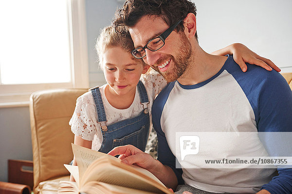 Mittlerer Erwachsener Mann liest Buch mit Tochter auf Sofa