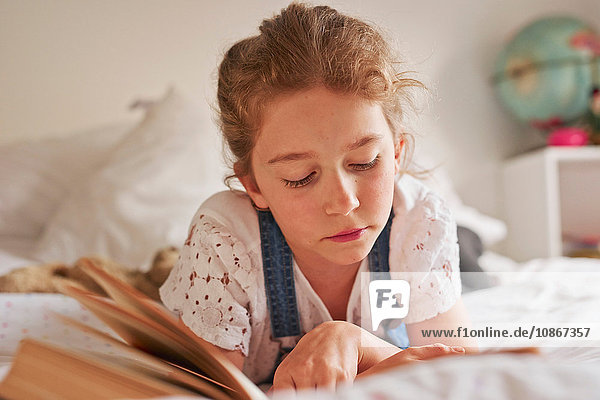 Mädchen liegt auf Bett und liest Buch
