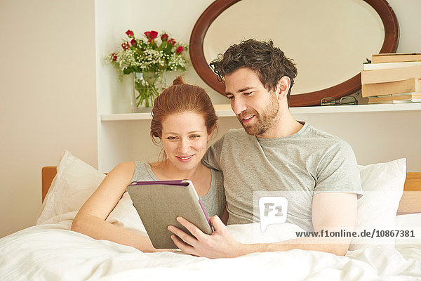 Mittelgroßes erwachsenes Paar beim Surfen auf dem digitalen Tablet im Bett