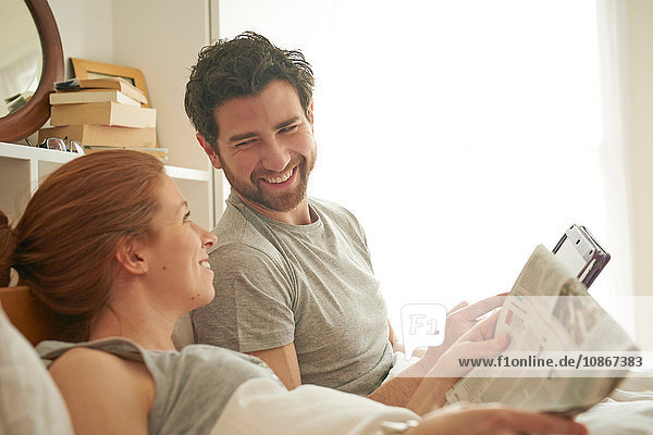Mid adult couple reading broadsheet and digital tablet in bed