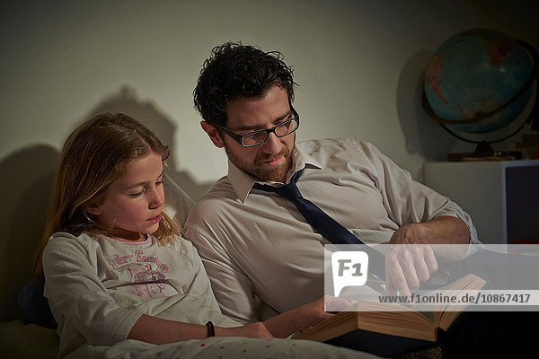 Geschäftsmann liest seiner Tochter zur Schlafenszeit ein Märchenbuch vor