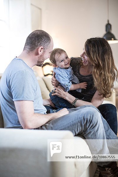 Parents sitting on sofa playing with smiling baby boy