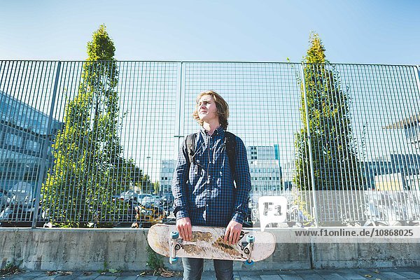Porträt eines jungen männlichen Skateboardfahrers mit Skateboard auf dem Bürgersteig