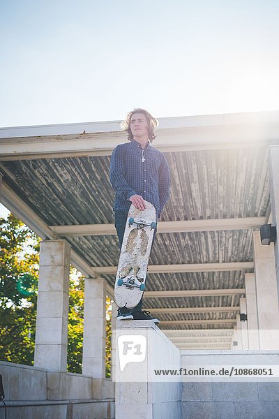 Porträt eines jungen männlichen Skateboardfahrers an der Wand stehend mit Skateboard