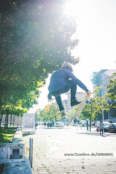 Junger männlicher Skateboarder beim Skateboarden Sprung auf dem Bürgersteig