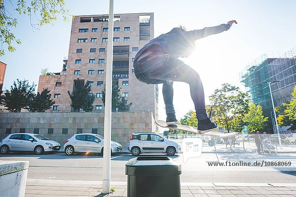 Junge männliche Skateboarder skateboarden über den Bürgersteig Mülleimer