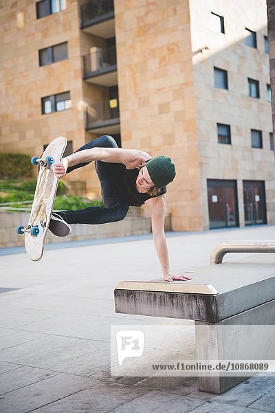 Junger männlicher Skateboarder beim Balance-Skateboard-Trick auf dem Sitz der Stadthalle