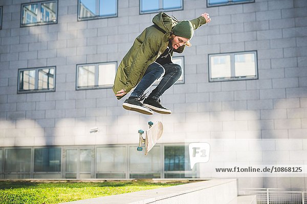 Junge männliche Skateboarder aus der Stadt skateboarden in der Luft über der Wand