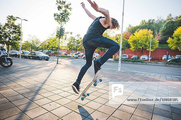 Young male urban skateboarder doing skateboarding jump trick on sidewalk