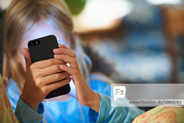 Junges Mädchen schaut auf ein Smartphone  das Gesicht wird vom Schein des Bildschirms beleuchtet