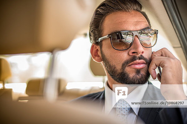 Junger Geschäftsmann mit Sonnenbrille spricht auf Smartphone auf dem Rücksitz eines Autos  Dubai  Vereinigte Arabische Emirate
