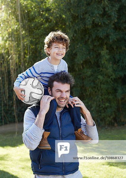 Father carrying smiling son holding football on shoulders
