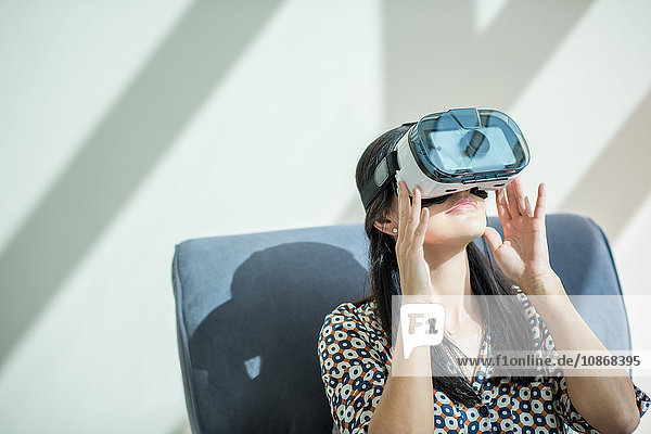 Frau auf Sessel schaut durch Virtual-Reality-Headset