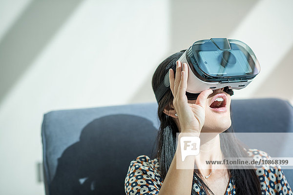 Frau mit offenem Mund auf Sessel schaut durch Virtual-Reality-Headset