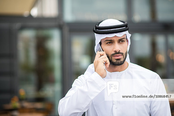 Mann mit Dishdasha läuft auf der Straße und unterhält sich per Smartphone  Dubai  Vereinigte Arabische Emirate