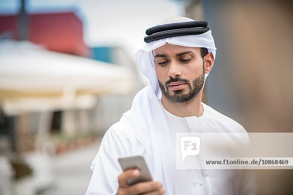 Mann in traditioneller Kleidung aus dem Nahen Osten liest Smartphone-Text  Dubai  Vereinigte Arabische Emirate
