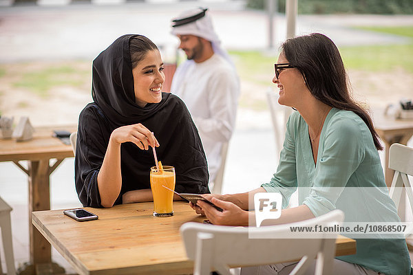 Junge Frau aus dem Nahen Osten in traditioneller Kleidung im Gespräch mit einer Freundin im Café  Dubai  Vereinigte Arabische Emirate
