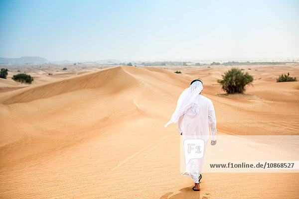 Rückansicht eines Mannes aus dem Nahen Osten  der in traditioneller Kleidung in der Wüste spazieren geht  Dubai  Vereinigte Arabische Emirate