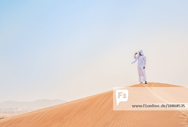 Mann aus dem Nahen Osten in traditioneller Kleidung mit Blick von Wüstendüne  Dubai  Vereinigte Arabische Emirate