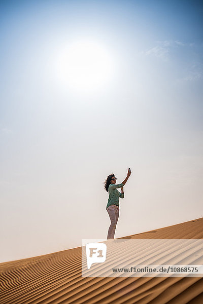 Woman tourist taking smartphone selfie on desert dune  Dubai  United Arab Emirates