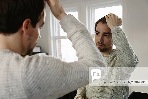 Mittelgroßer erwachsener Mann  der in den Spiegel schaut und seine Haare kontrolliert