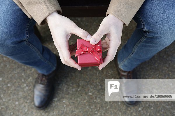 Mann sitzt im Freien  hält kleine rote Schachtel  Draufsicht  Nahaufnahme