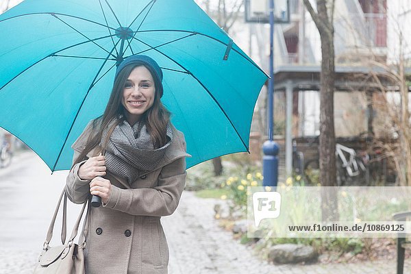 Porträt einer jungen Frau im Freien  die einen blauen Regenschirm hält