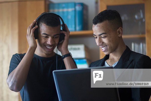 Zwillingsbrüder zu Hause  schauen auf den Laptop  tragen Kopfhörer  lächeln