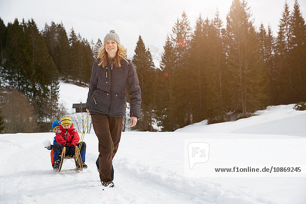Frau zieht Söhne auf Schlitten in schneebedeckter Landschaft  Elmau  Bayern  Deutschland