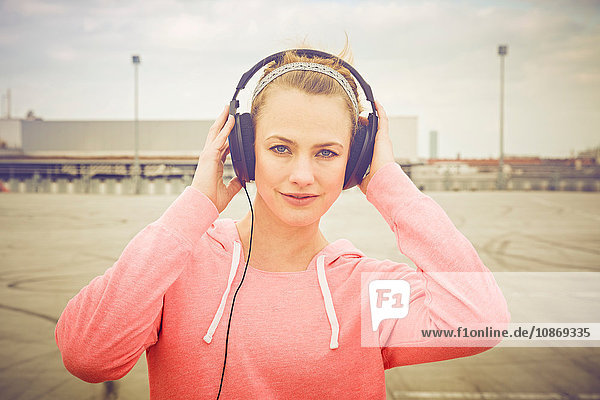 Porträt einer Frau mit Händen über Kopfhörer beim Musikhören auf dem Parkplatz auf dem Dach
