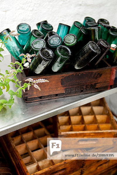 Holzkiste mit umgedrehten Vintage-Flaschen auf Terrasse bei Regen