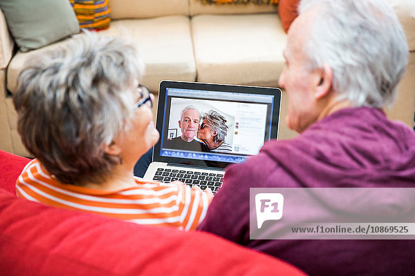 Über-Schulter-Ansicht eines älteren Paares auf einem Wohnzimmersofa beim Betrachten von Fotos auf einem Laptop