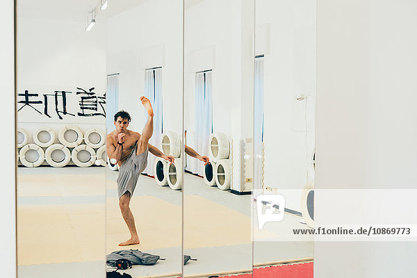 Mirror image of martial artist in gym doing kick