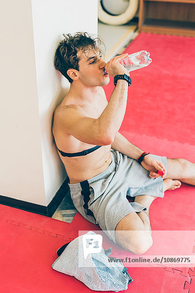 Man sitting leaning against column wearing heart rate monitor on chest  drinking water from bottle