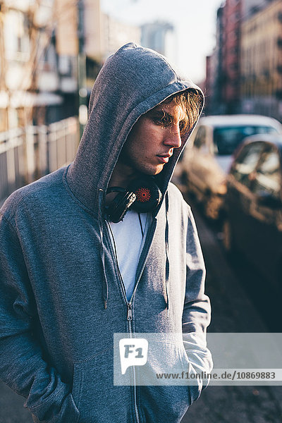 Man wearing hooded top and headphones  hands in pockets looking away