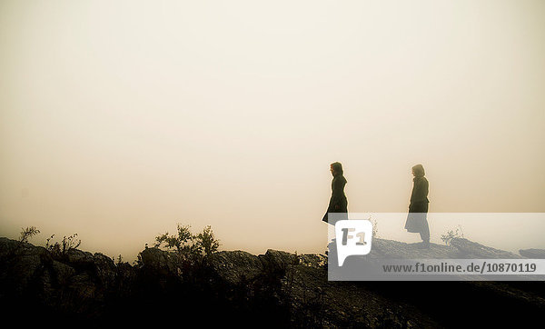 Side view of couple wearing raincoats standing on rocks in fog looking away