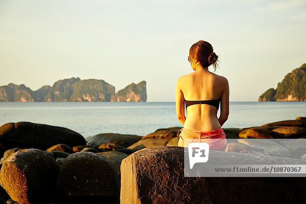 Junge Frau sitzt auf einem Küstenfelsen  Phi Phi-Inseln  Thailand