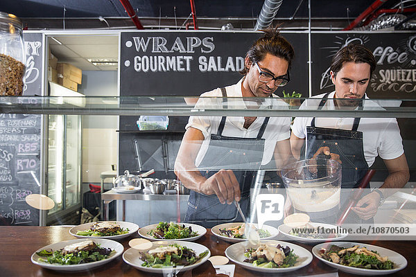 Restaurateurs preparing salad behind service counter