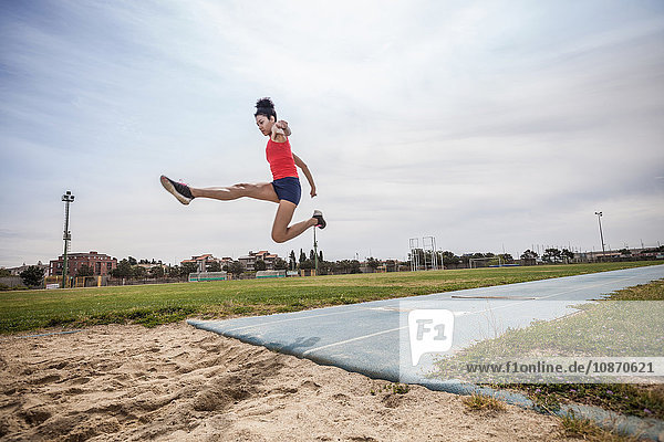 Junge weibliche Weitspringerin springt in der Luft auf Sportanlage