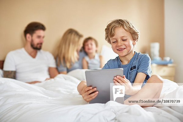 Boy on parents bed using digital tablet smiling