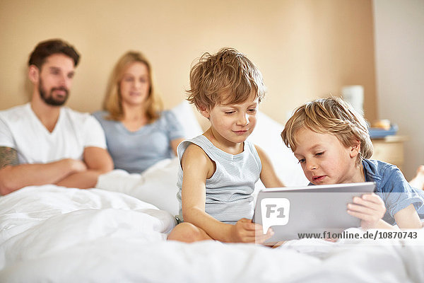 Jungen im Bett der Eltern mit digitalem Tablett