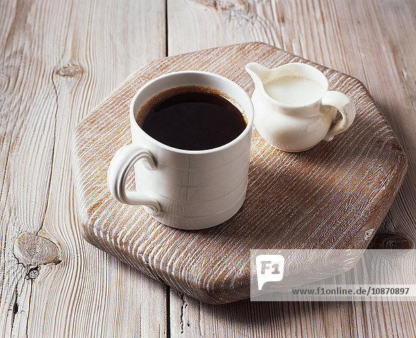 Tasse schwarzer Kaffee und Milchkännchen auf Schneidebrett