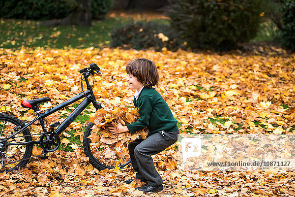 Junge im Park mit Fahrrad im Herbstlaub spielend